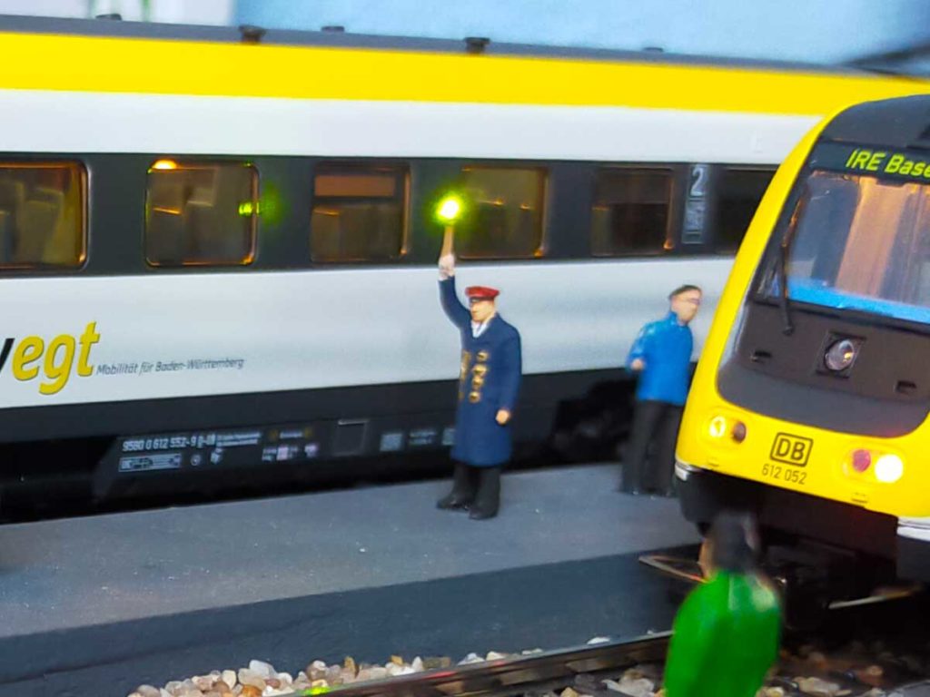 Abertigung eines Zuges auf der Modellbahn mit leuchtender Kelle des Bahnpersonals